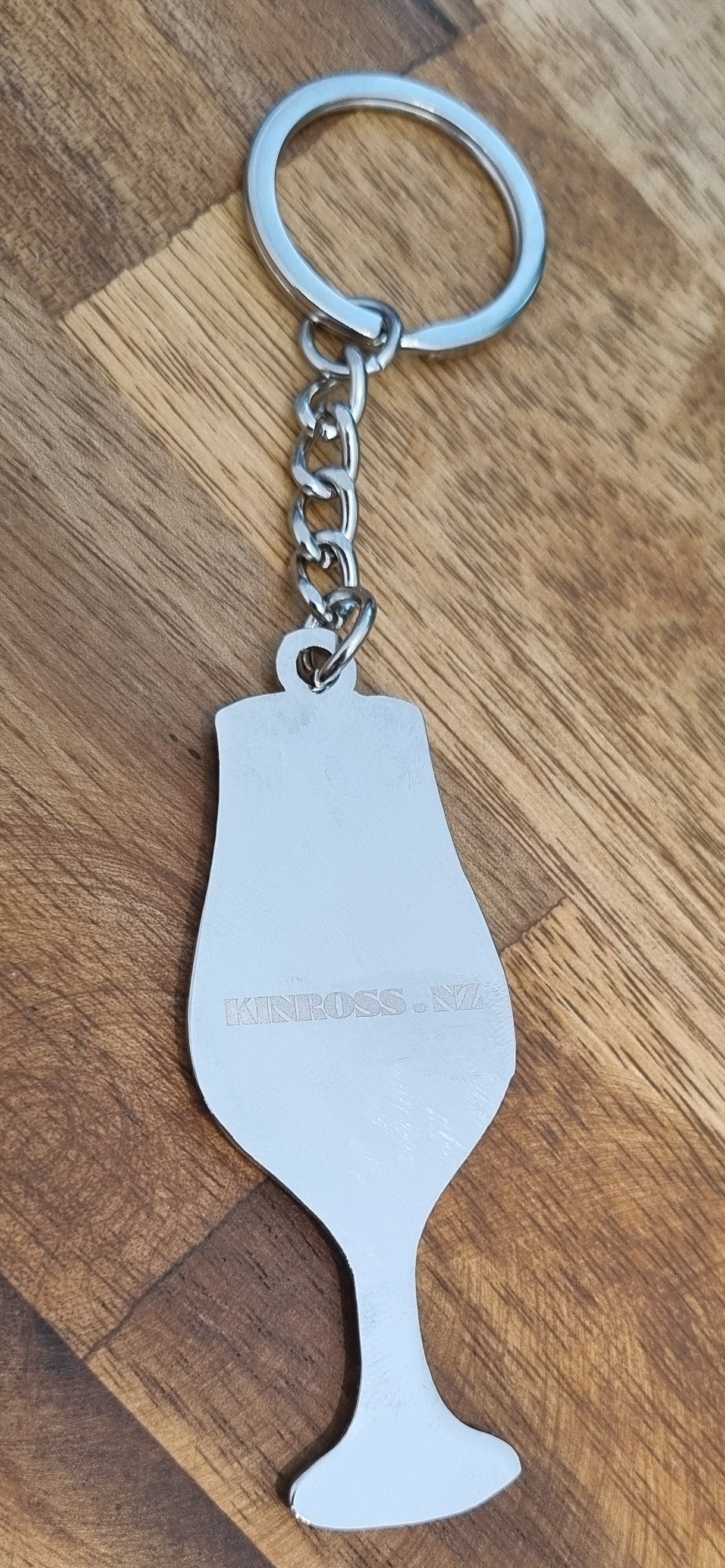 Metallic wine glass-shaped keychain on a wooden surface