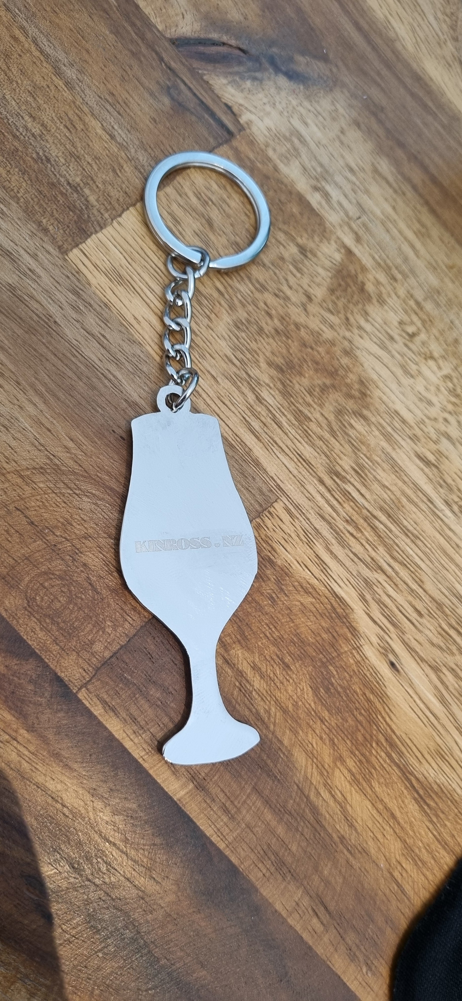 Metallic wine glass-shaped keychain on a wooden surface